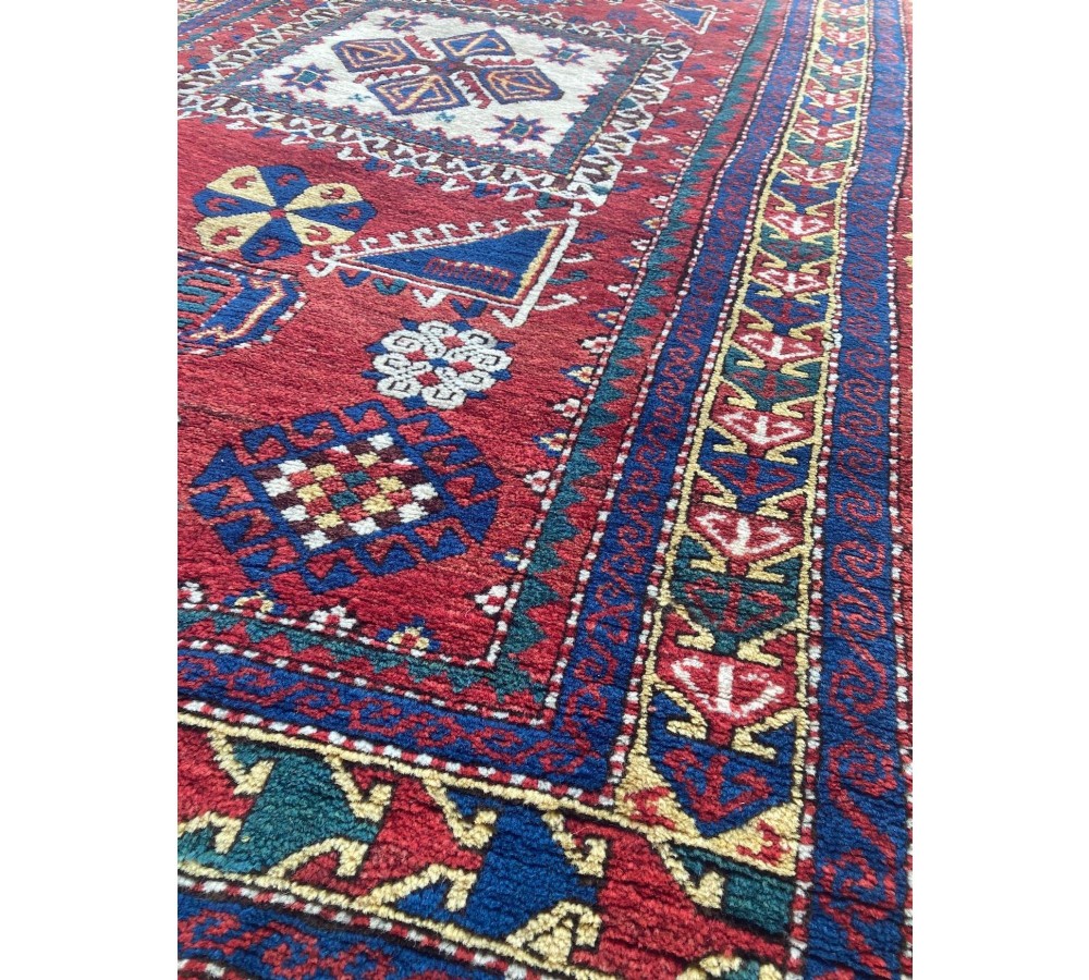 A hand-knotted Caucasian prayer rug featuring a red central field with a pointed mihrab niche, geometric medallions, and multi-band patterned borders in navy blue, red, and cream. View VIII