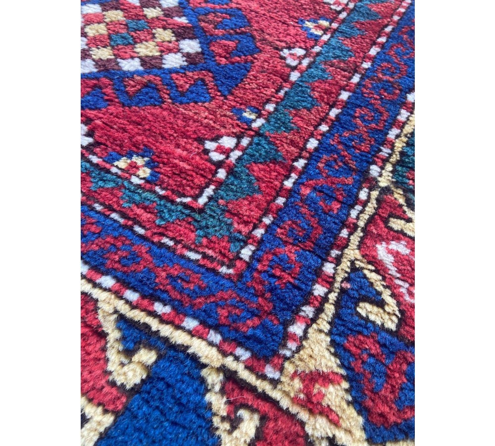A hand-knotted Caucasian prayer rug featuring a red central field with a pointed mihrab niche, geometric medallions, and multi-band patterned borders in navy blue, red, and cream. View IX