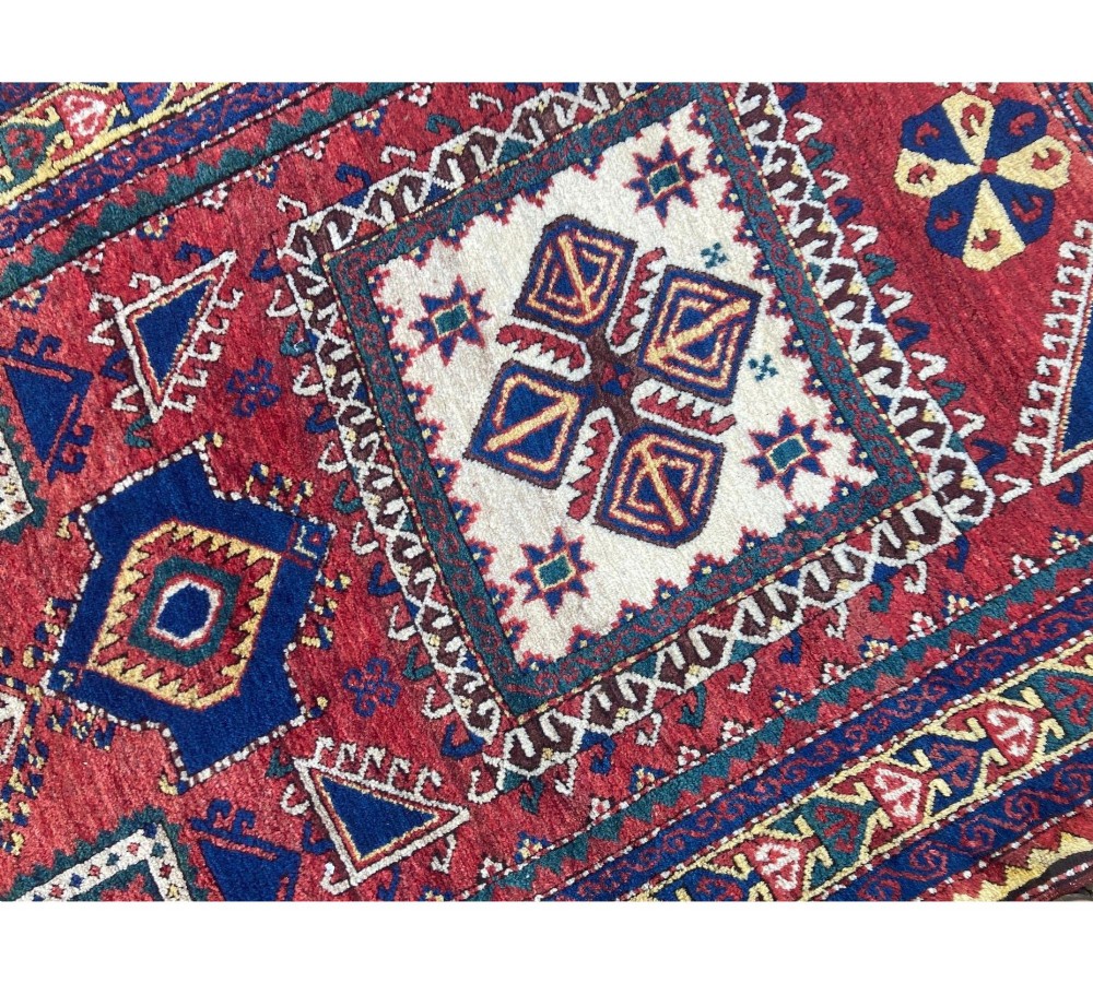 A hand-knotted Caucasian prayer rug featuring a red central field with a pointed mihrab niche, geometric medallions, and multi-band patterned borders in navy blue, red, and cream. View X