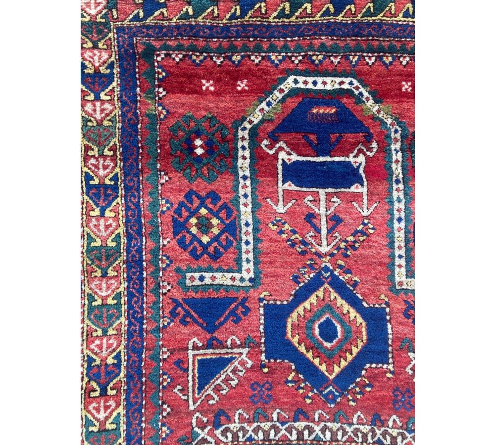 A hand-knotted Caucasian prayer rug featuring a red central field with a pointed mihrab niche, geometric medallions, and multi-band patterned borders in navy blue, red, and cream. View XI