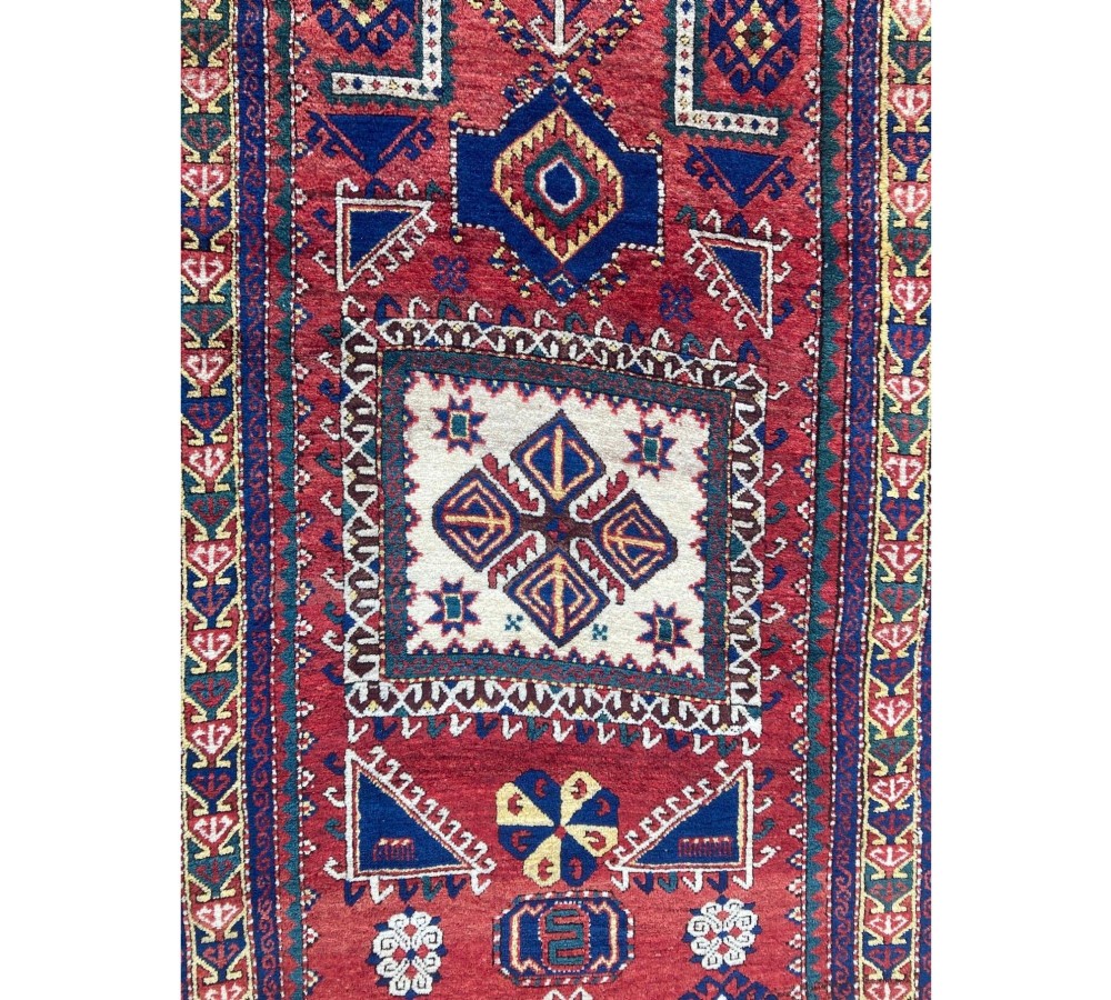 A hand-knotted Caucasian prayer rug featuring a red central field with a pointed mihrab niche, geometric medallions, and multi-band patterned borders in navy blue, red, and cream. View XIII