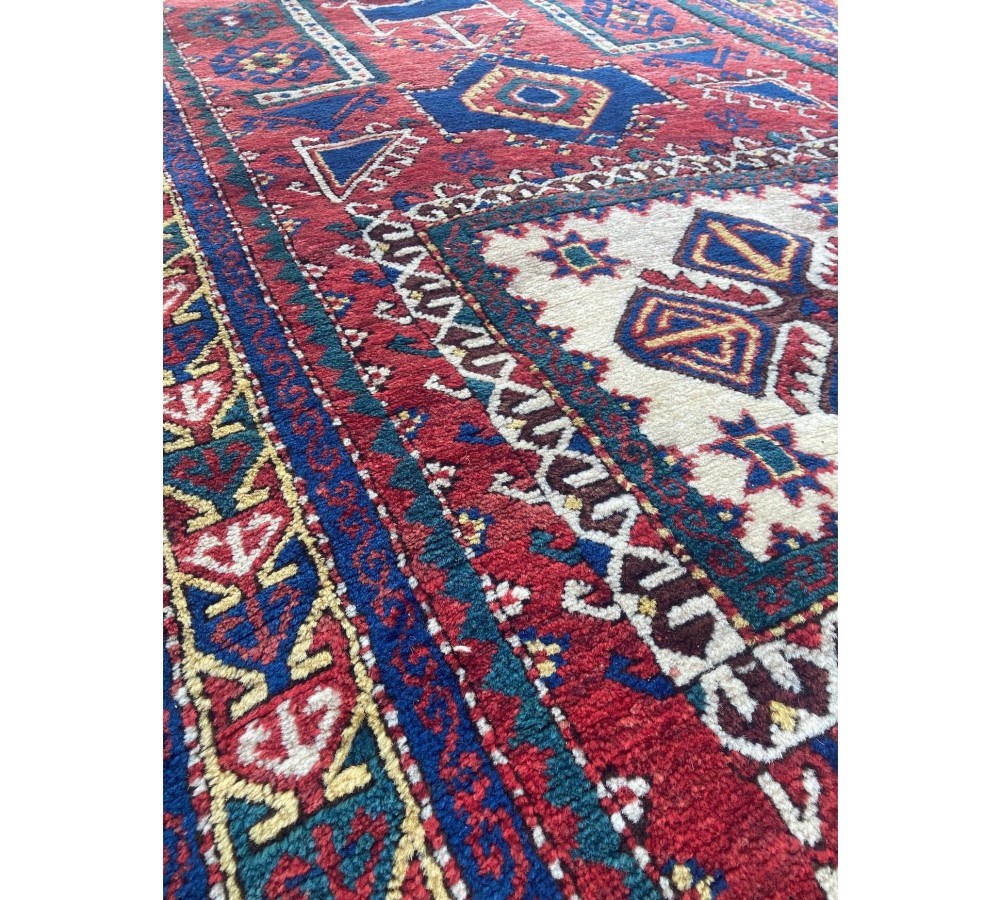 A hand-knotted Caucasian prayer rug featuring a red central field with a pointed mihrab niche, geometric medallions, and multi-band patterned borders in navy blue, red, and cream. View XIV