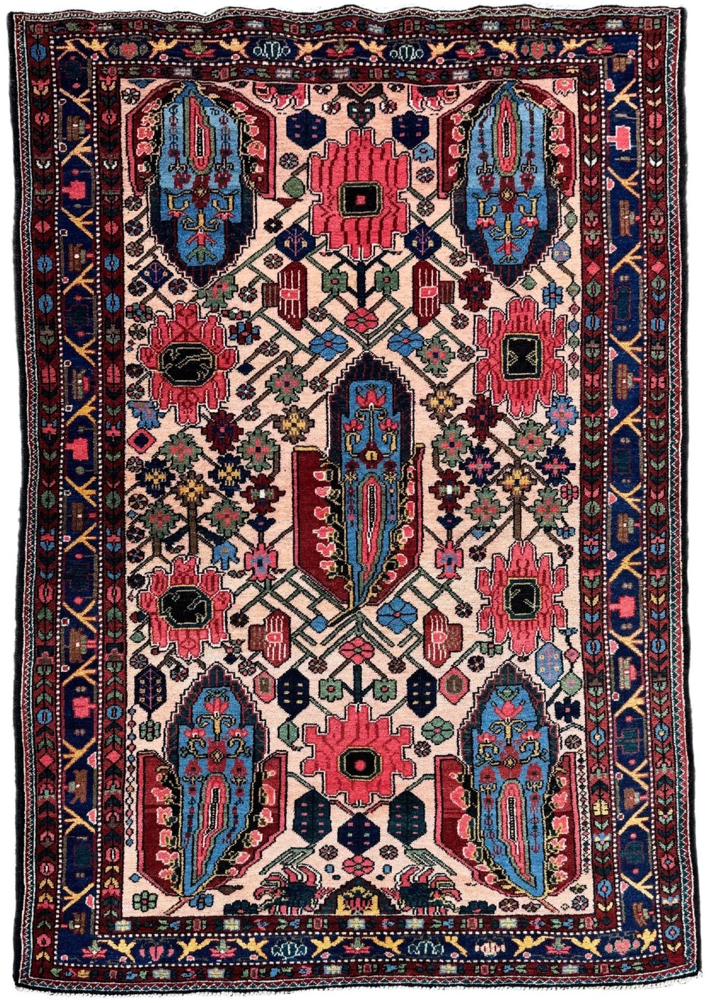 An antique Persian Bakhtiar wool rug featuring intricate geometric floral patterns and bird motifs in blue, pink, and red set against a cream background with a dark blue decorative border.