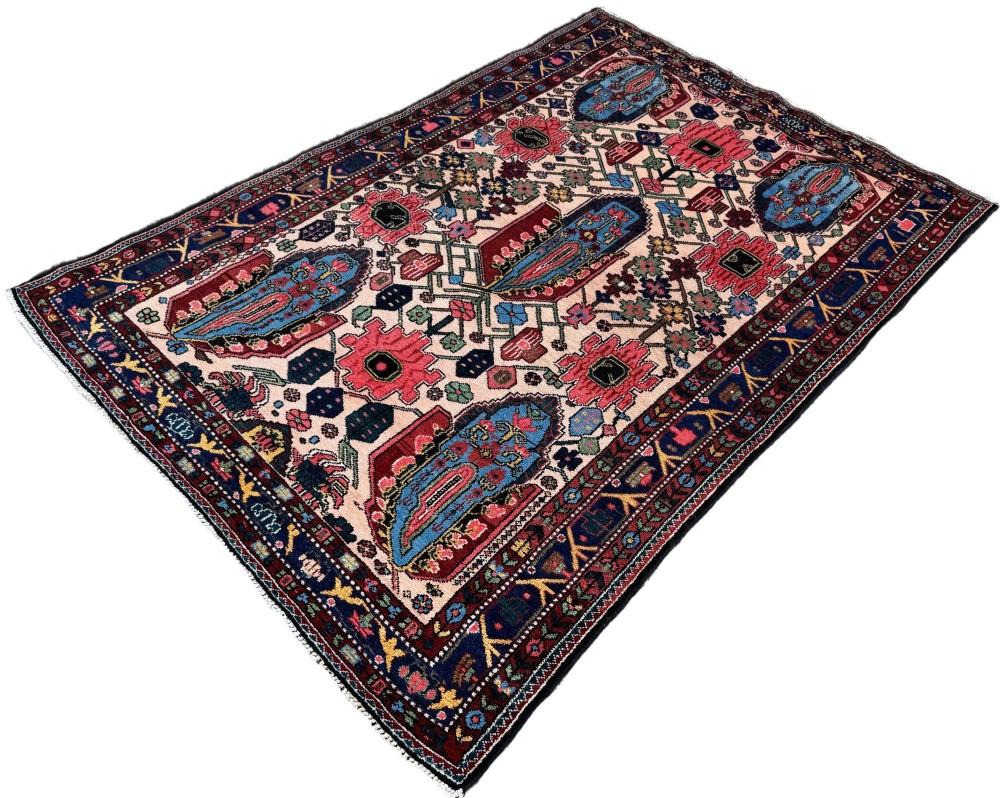 An antique Persian Bakhtiar wool rug featuring intricate geometric floral patterns and bird motifs in blue, pink, and red set against a cream background with a dark blue decorative border. View III