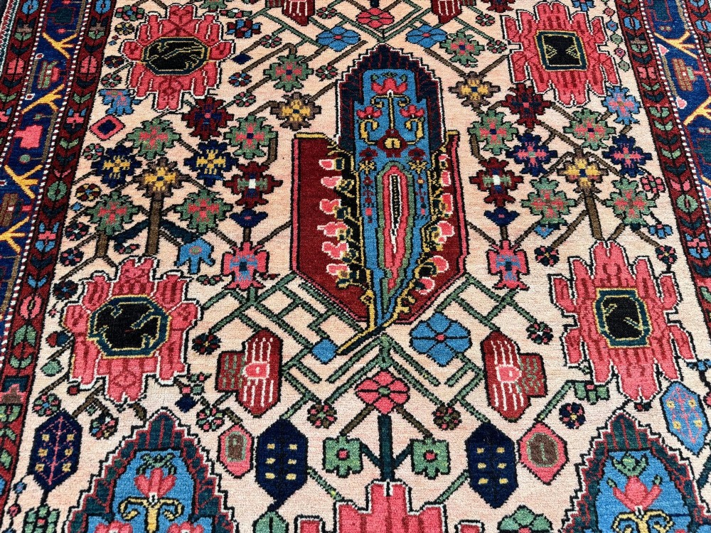An antique Persian Bakhtiar wool rug featuring intricate geometric floral patterns and bird motifs in blue, pink, and red set against a cream background with a dark blue decorative border. View VIII