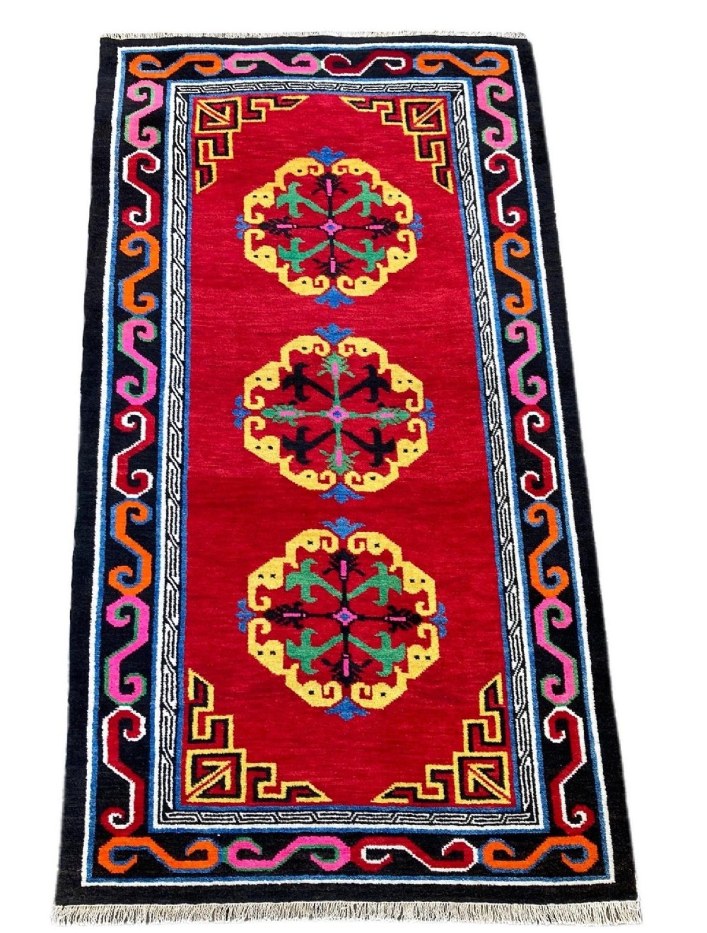 A hand-knotted rectangular Tibetan wool rug featuring a bright red centre field with three yellow and green central medallion motifs framed by a black cloud-scroll border. View II