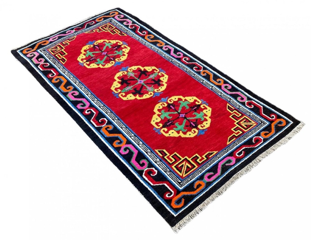 A hand-knotted rectangular Tibetan wool rug featuring a bright red centre field with three yellow and green central medallion motifs framed by a black cloud-scroll border. View III