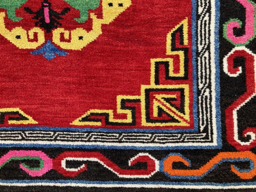 A hand-knotted rectangular Tibetan wool rug featuring a bright red centre field with three yellow and green central medallion motifs framed by a black cloud-scroll border. View V