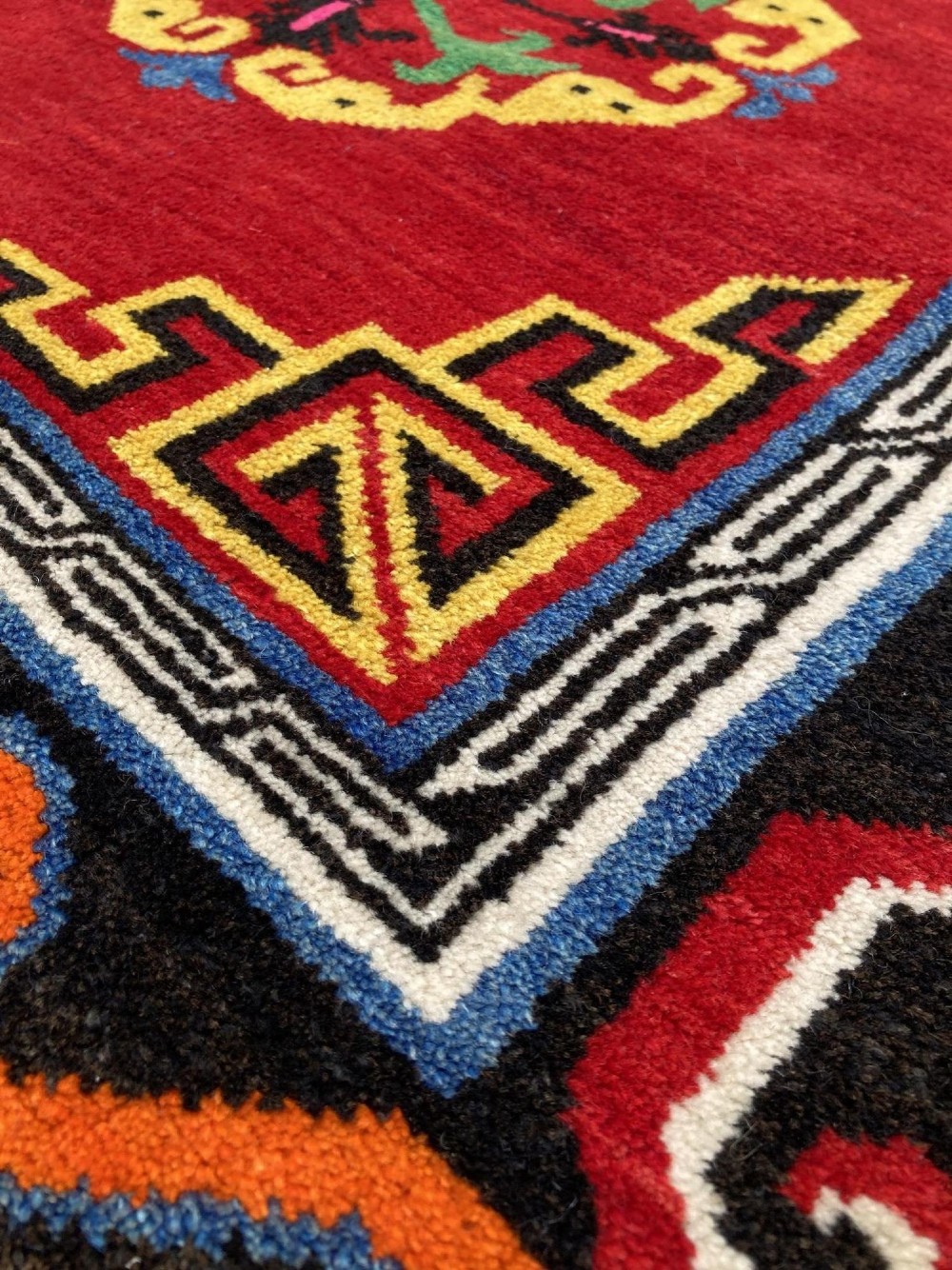 A hand-knotted rectangular Tibetan wool rug featuring a bright red centre field with three yellow and green central medallion motifs framed by a black cloud-scroll border. View VIII