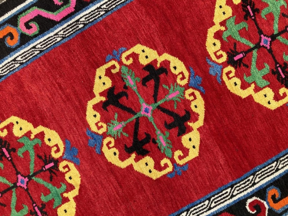 A hand-knotted rectangular Tibetan wool rug featuring a bright red centre field with three yellow and green central medallion motifs framed by a black cloud-scroll border. View IX