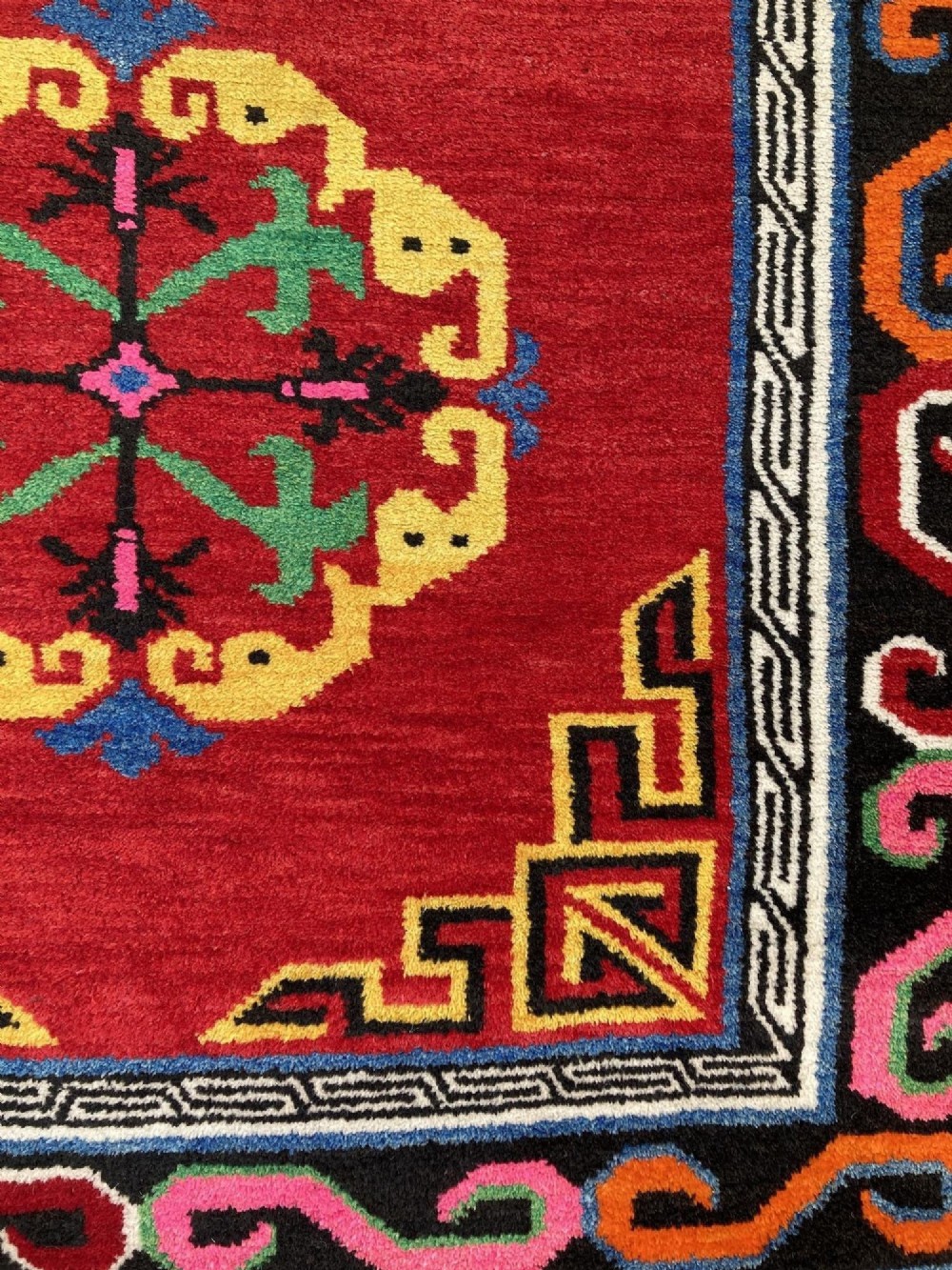 A hand-knotted rectangular Tibetan wool rug featuring a bright red centre field with three yellow and green central medallion motifs framed by a black cloud-scroll border. View X