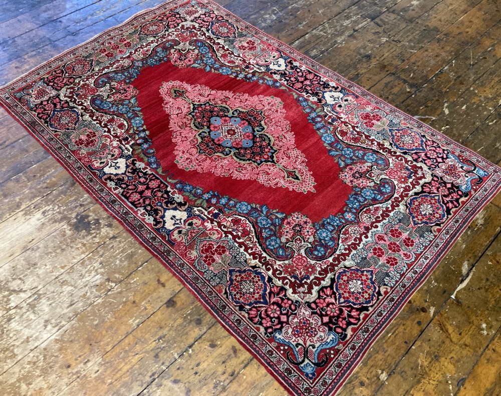 Hand-knotted antique Persian Sarouk wool rug featuring a large central floral medallion on a rich red ground with elaborate decorative borders. View V