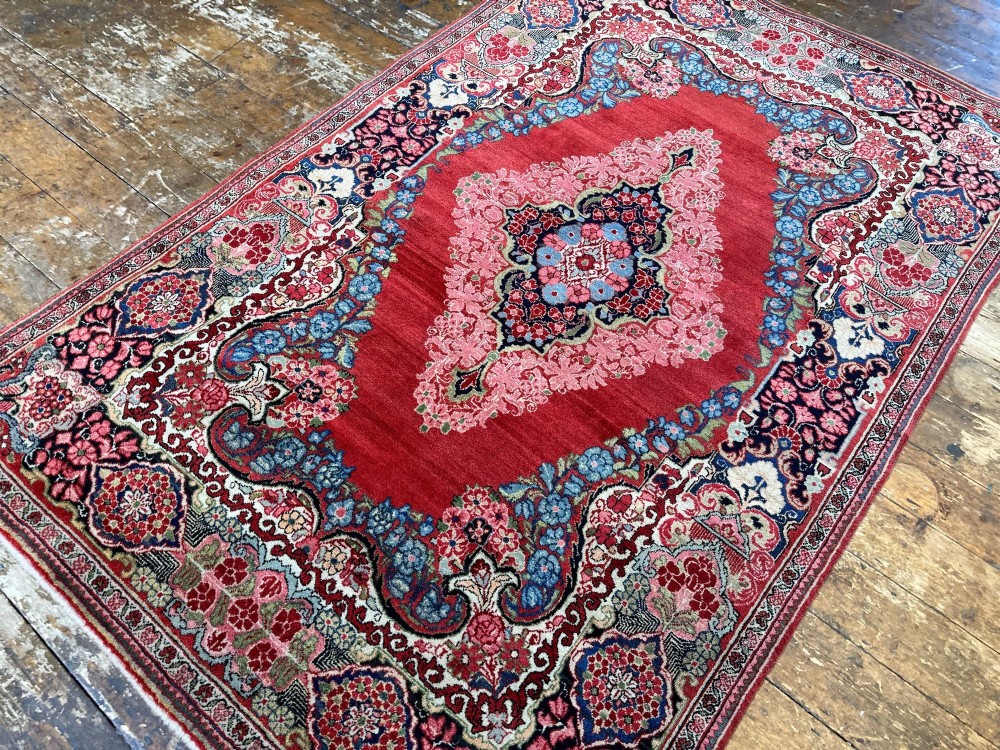 Hand-knotted antique Persian Sarouk wool rug featuring a large central floral medallion on a rich red ground with elaborate decorative borders. View VI