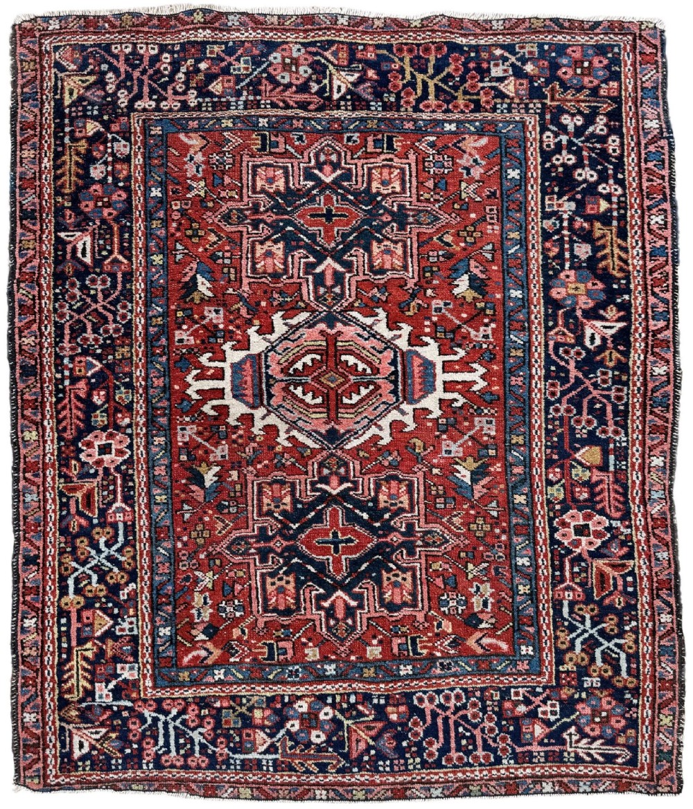 An antique hand-knotted Karaja rug featuring three geometric central medallions in pink, blue, and navy on a crimson red field surrounded by a dark navy border.