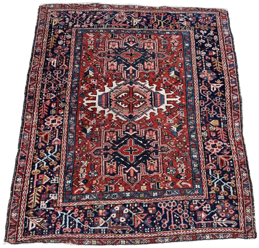An antique hand-knotted Karaja rug featuring three geometric central medallions in pink, blue, and navy on a crimson red field surrounded by a dark navy border. View II