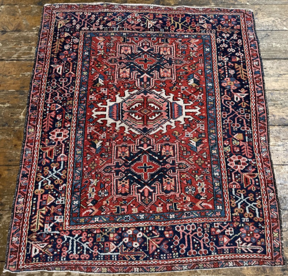 An antique hand-knotted Karaja rug featuring three geometric central medallions in pink, blue, and navy on a crimson red field surrounded by a dark navy border. View IV