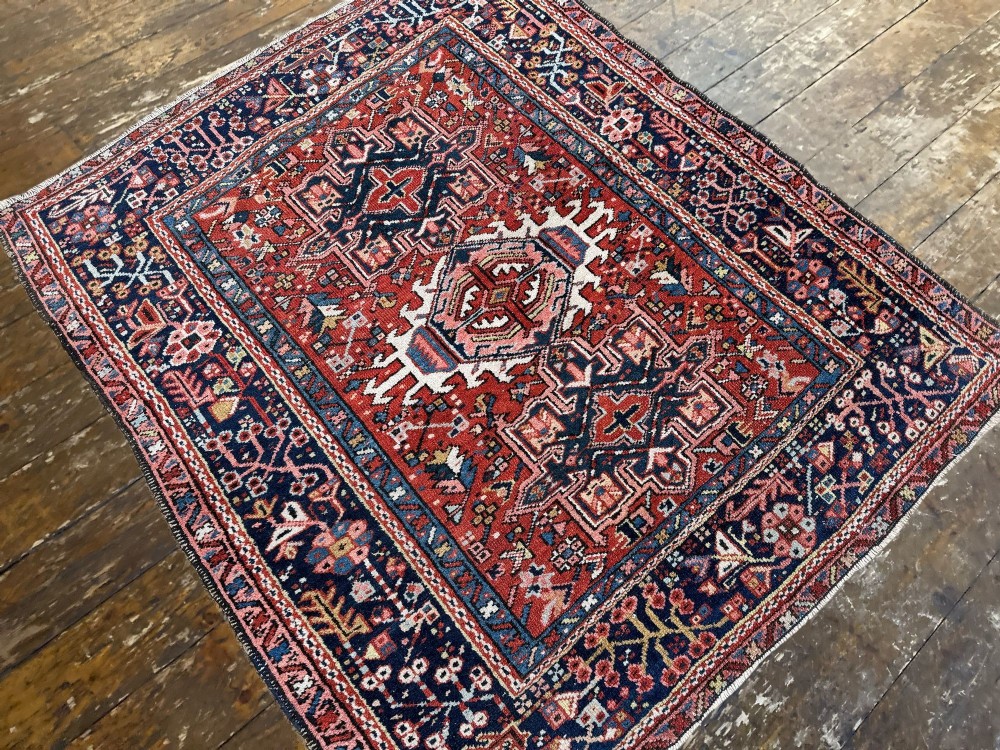An antique hand-knotted Karaja rug featuring three geometric central medallions in pink, blue, and navy on a crimson red field surrounded by a dark navy border. View VI