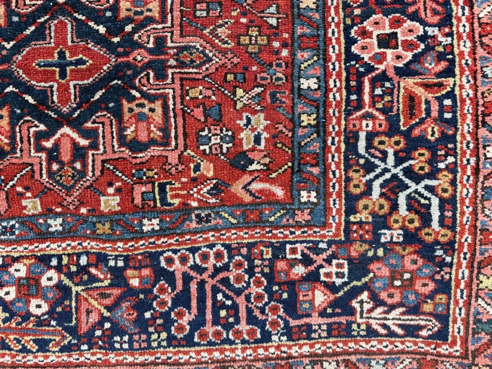 An antique hand-knotted Karaja rug featuring three geometric central medallions in pink, blue, and navy on a crimson red field surrounded by a dark navy border. View VII