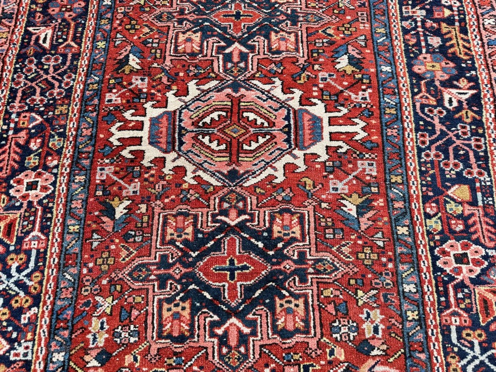 An antique hand-knotted Karaja rug featuring three geometric central medallions in pink, blue, and navy on a crimson red field surrounded by a dark navy border. View VIII