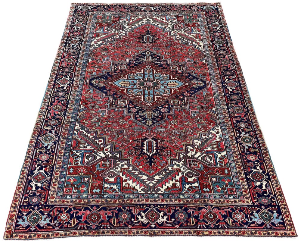 A large hand-knotted antique Heriz wool carpet featuring a prominent central geometric medallion on a deep red field framed by dark navy and cream borders. View II
