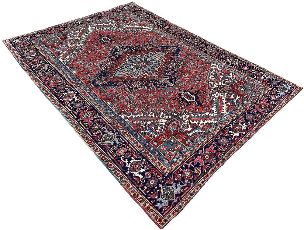 A large hand-knotted antique Heriz wool carpet featuring a prominent central geometric medallion on a deep red field framed by dark navy and cream borders. View III