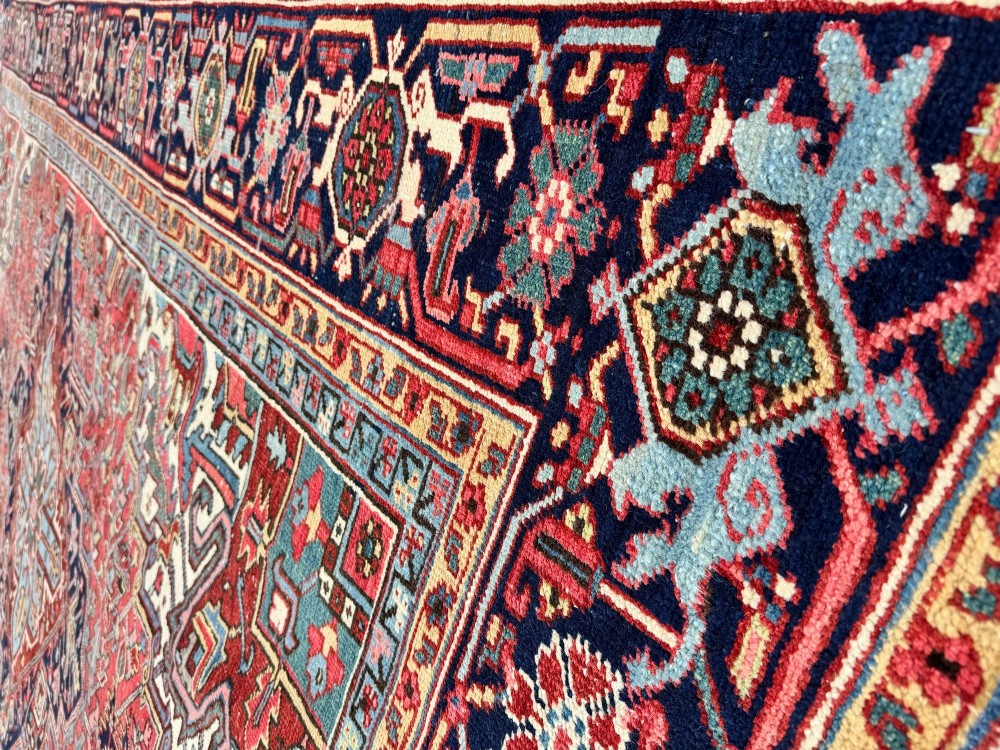 A large hand-knotted antique Heriz wool carpet featuring a prominent central geometric medallion on a deep red field framed by dark navy and cream borders. View IX