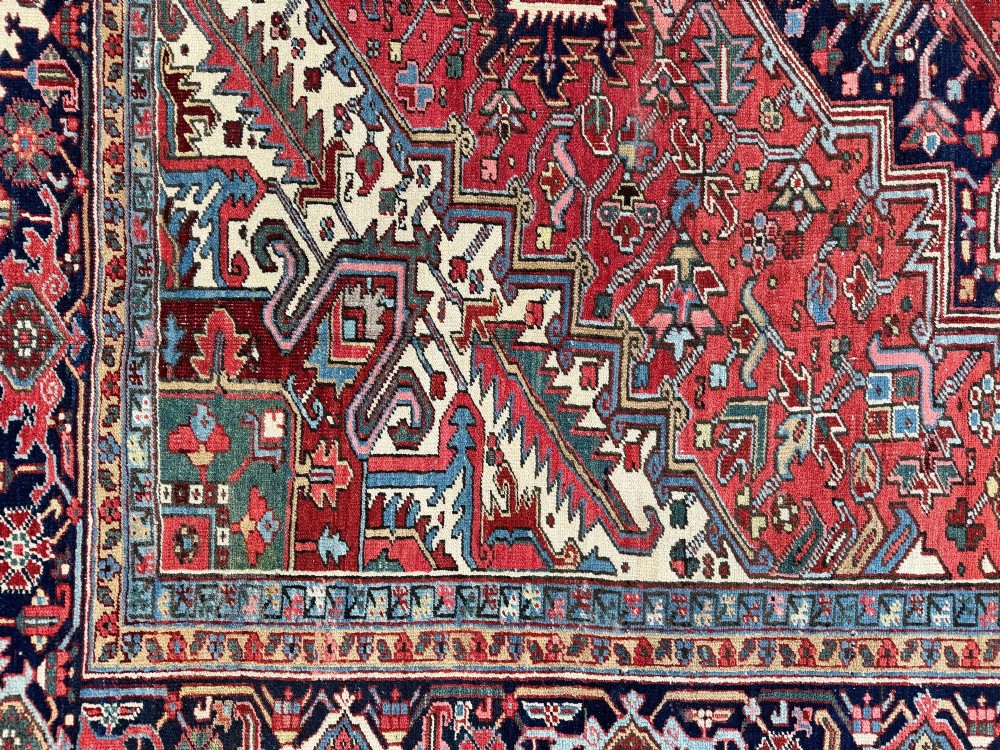 A large hand-knotted antique Heriz wool carpet featuring a prominent central geometric medallion on a deep red field framed by dark navy and cream borders. View XII