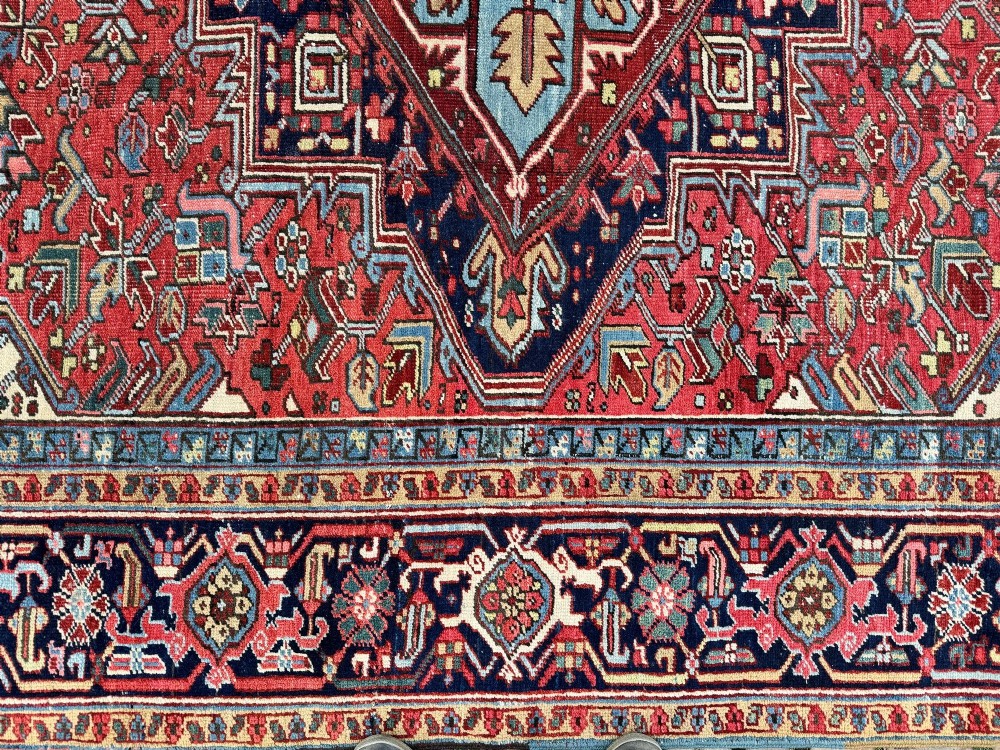 A large hand-knotted antique Heriz wool carpet featuring a prominent central geometric medallion on a deep red field framed by dark navy and cream borders. View XIII