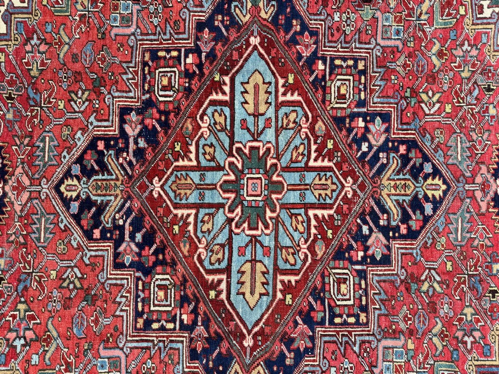 A large hand-knotted antique Heriz wool carpet featuring a prominent central geometric medallion on a deep red field framed by dark navy and cream borders. View XIV