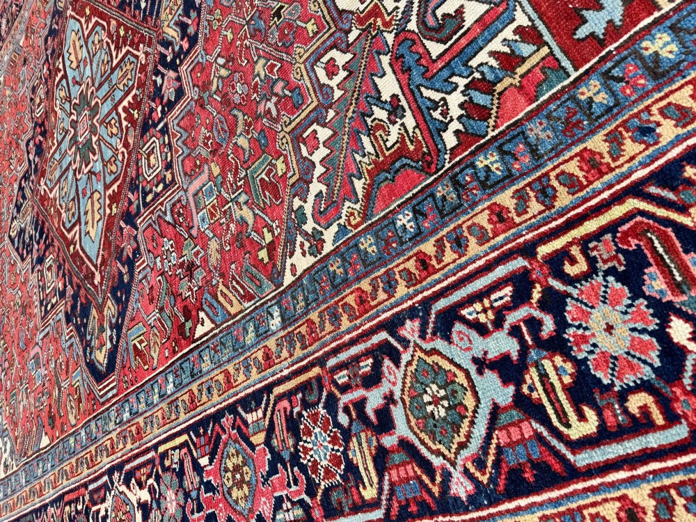 A large hand-knotted antique Heriz wool carpet featuring a prominent central geometric medallion on a deep red field framed by dark navy and cream borders. View XV