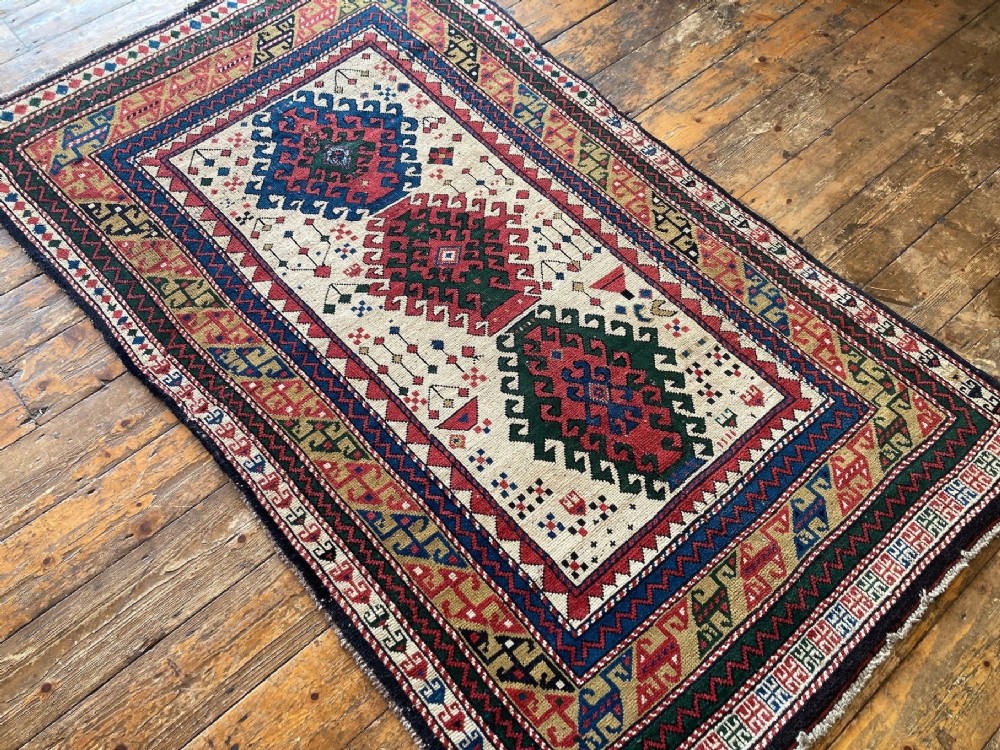 An antique hand-knotted Caucasian Kazak wool rug featuring three stacked geometric medallions on an ivory ground with multi-coloured geometric borders. View IV