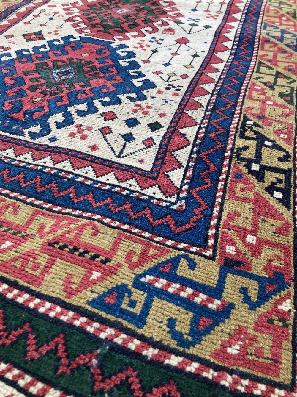 An antique hand-knotted Caucasian Kazak wool rug featuring three stacked geometric medallions on an ivory ground with multi-coloured geometric borders. View VII