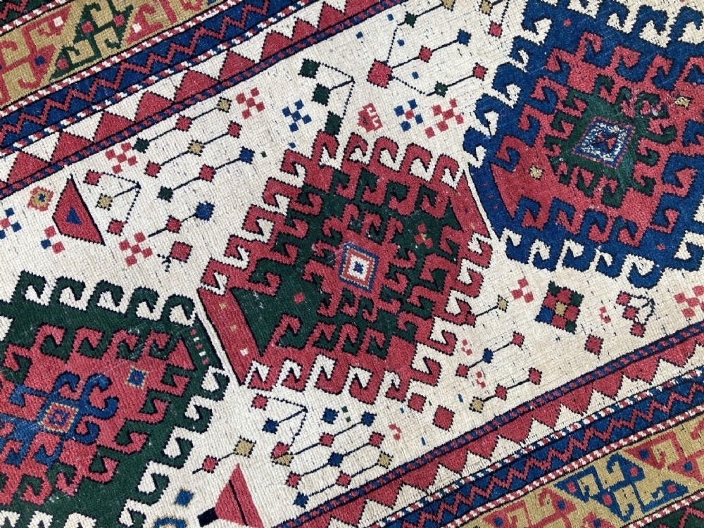 An antique hand-knotted Caucasian Kazak wool rug featuring three stacked geometric medallions on an ivory ground with multi-coloured geometric borders. View IX