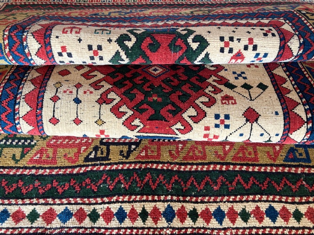 An antique hand-knotted Caucasian Kazak wool rug featuring three stacked geometric medallions on an ivory ground with multi-coloured geometric borders. View XIV