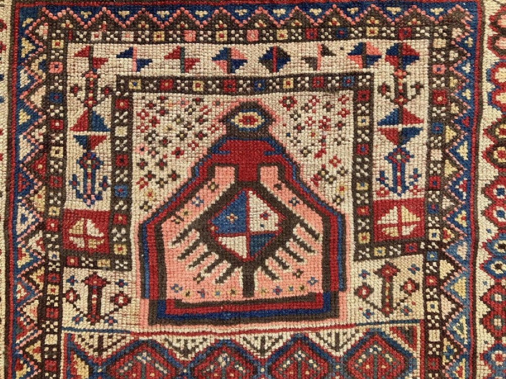 A hand-knotted antique Caucasian Gendje prayer rug featuring a deep red central field with a diamond lattice pattern, topped with a geometric mihrab motif and framed by multi-coloured decorative borders. View XI