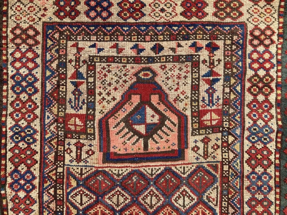 A hand-knotted antique Caucasian Gendje prayer rug featuring a deep red central field with a diamond lattice pattern, topped with a geometric mihrab motif and framed by multi-coloured decorative borders. View XII