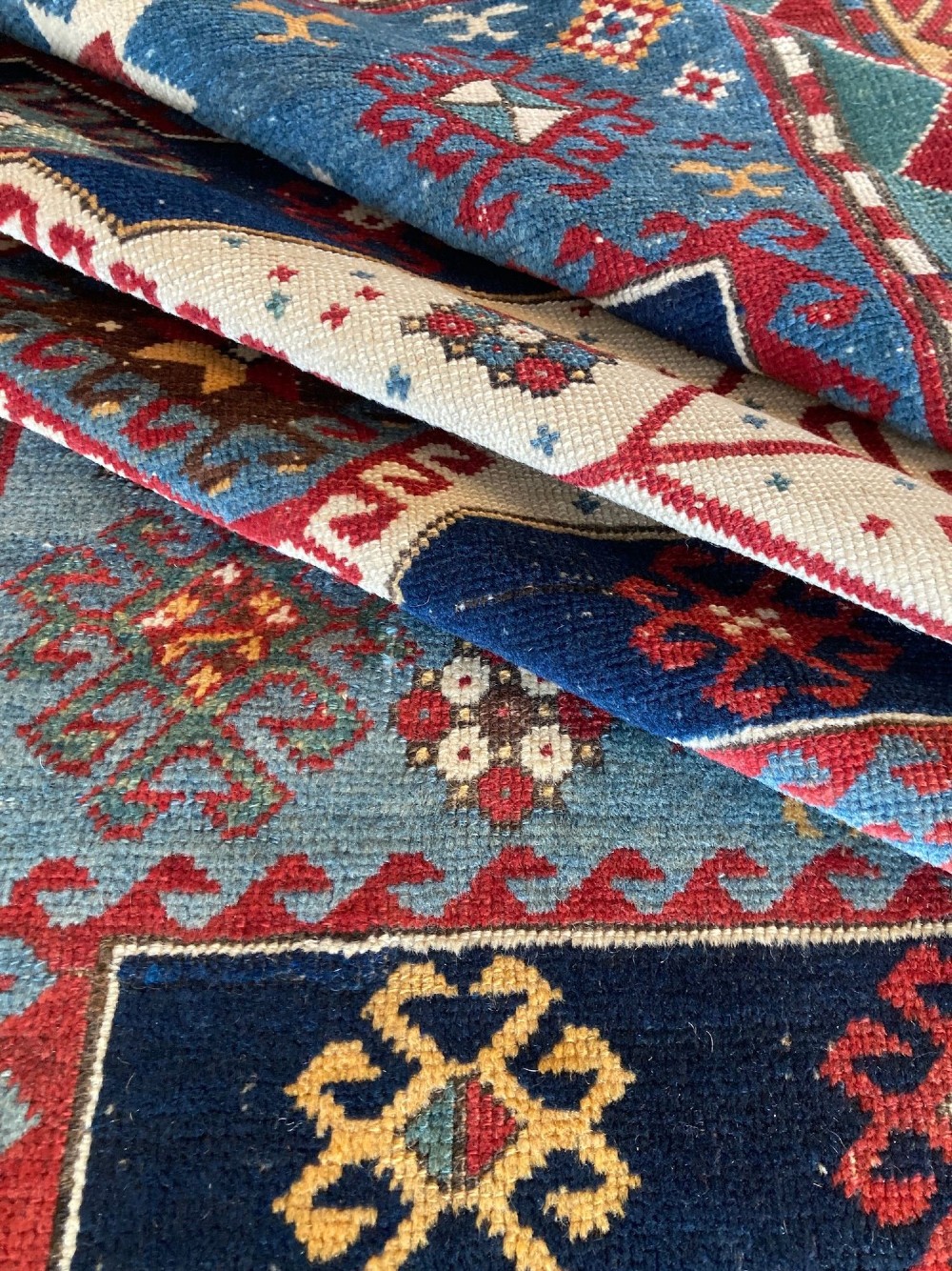 An antique Caucasian Kazak wool rug featuring three central geometric medallions surrounded by stylised animal figures and multi-tiered patterned borders in blue, red, cream, and yellow hues. View XV