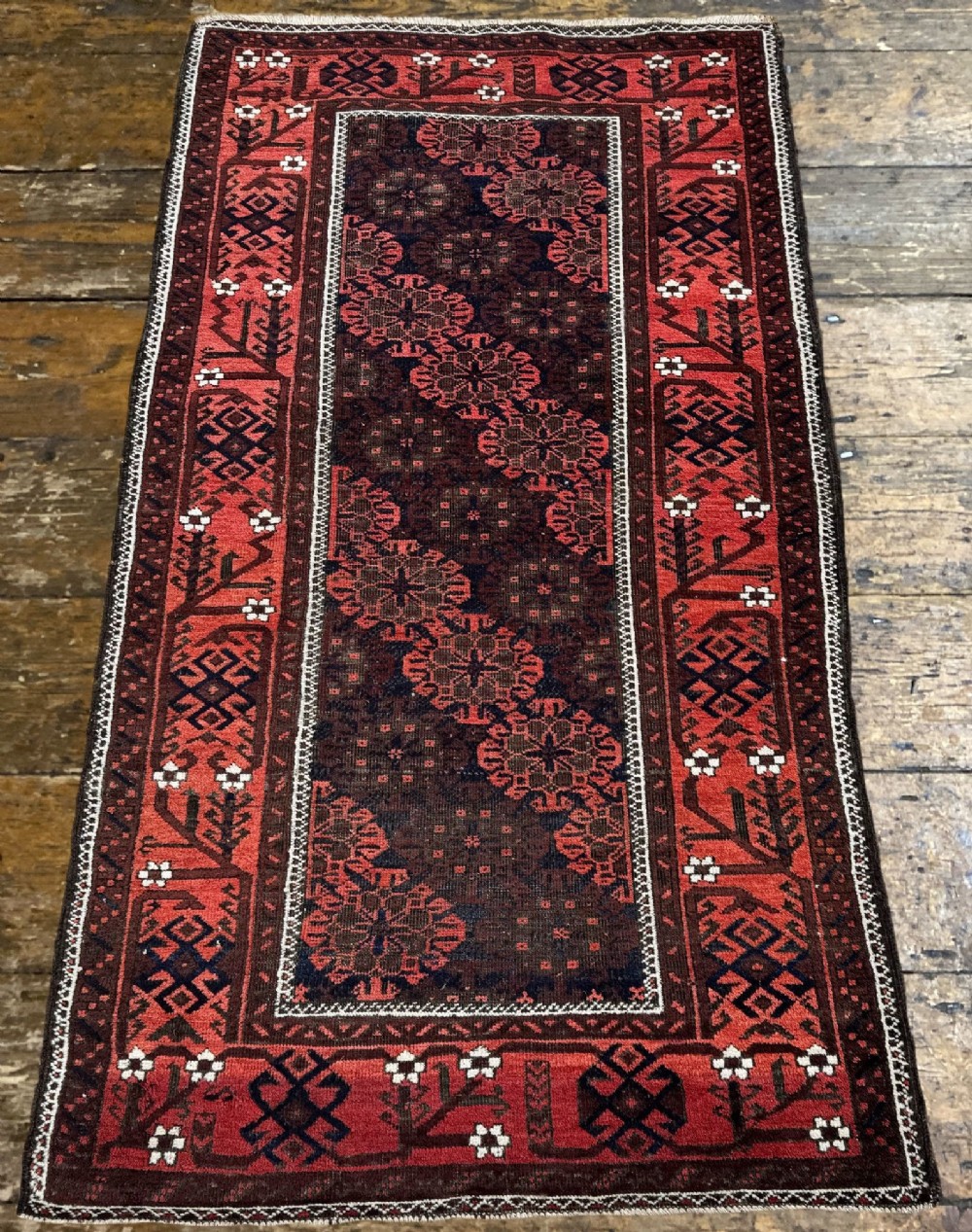An antique hand-knotted Belouch wool rug featuring geometric star motifs, a dark brown central field, and a deep red patterned border. View IV