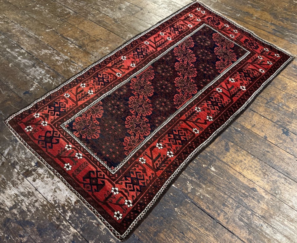An antique hand-knotted Belouch wool rug featuring geometric star motifs, a dark brown central field, and a deep red patterned border. View V