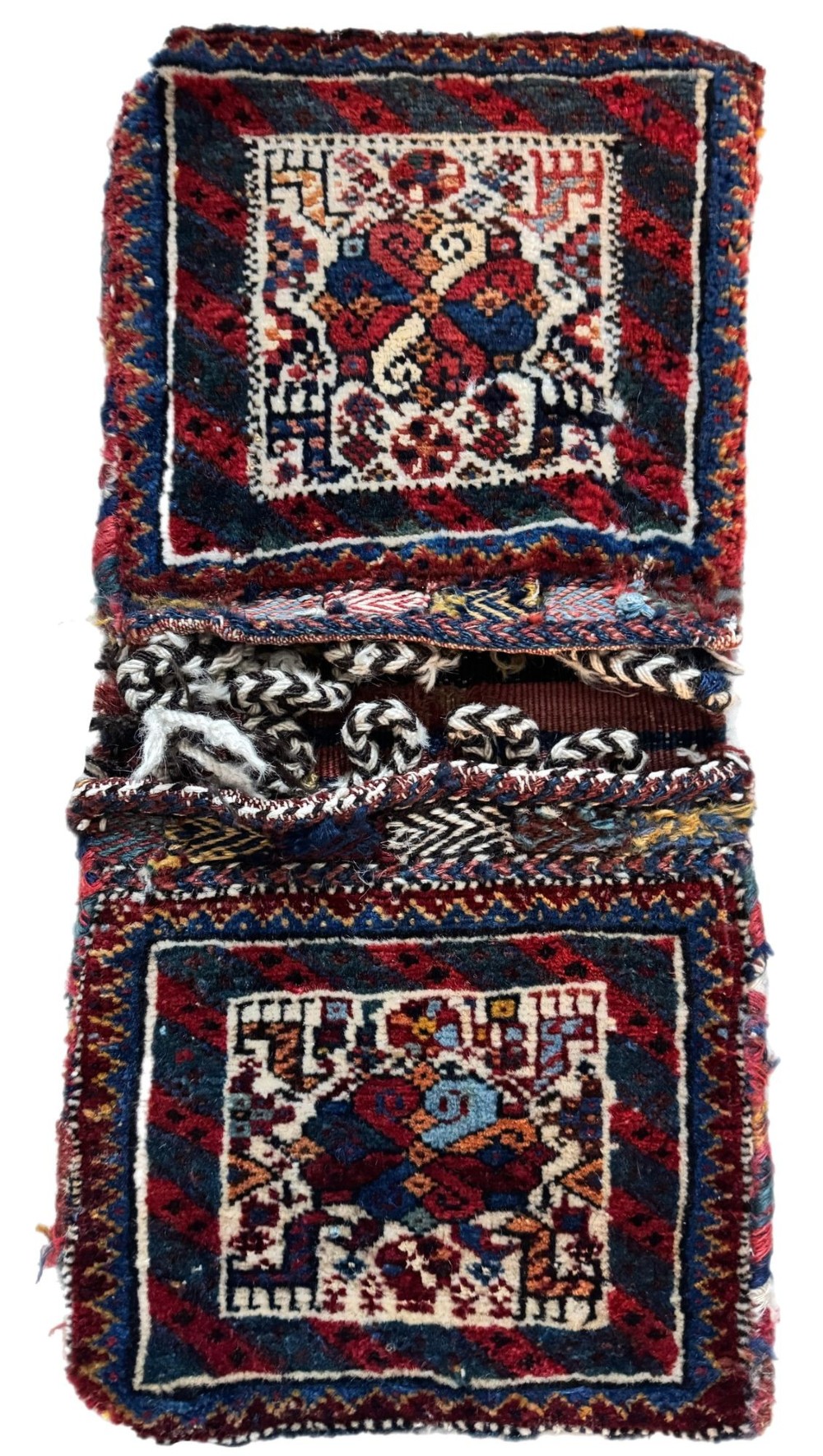 An antique handwoven Qashqai wool Khorjin double saddlebag featuring geometric medallions in red, navy, and cream with braided closure loops.