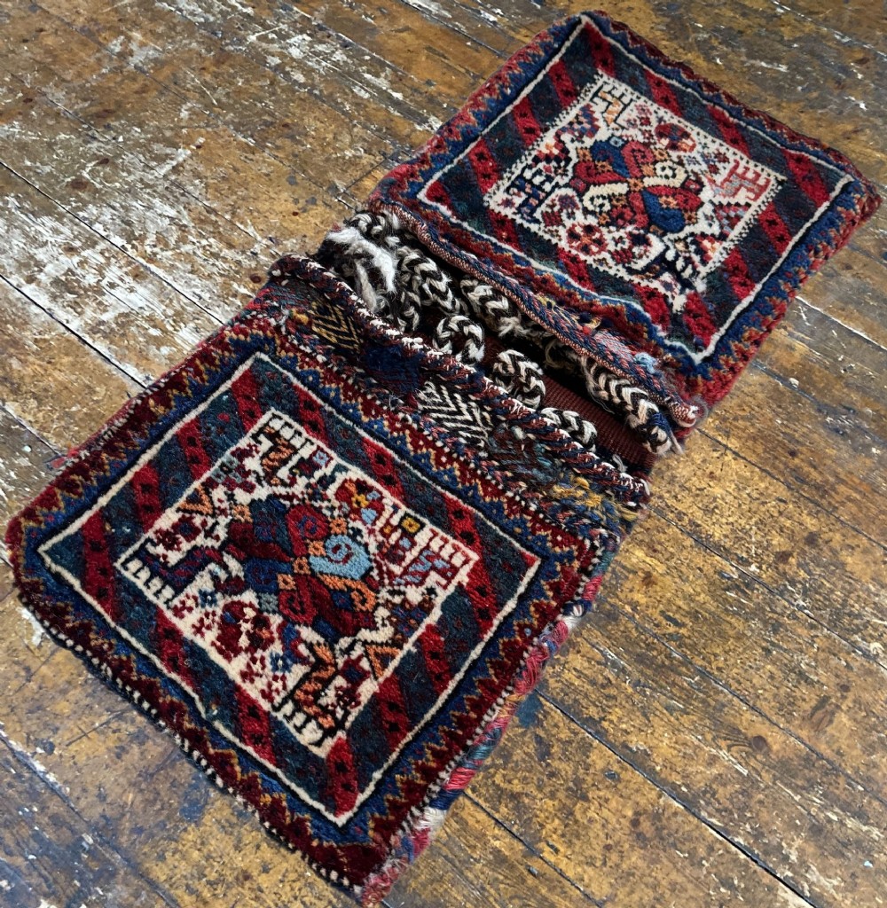 An antique handwoven Qashqai wool Khorjin double saddlebag featuring geometric medallions in red, navy, and cream with braided closure loops. View V