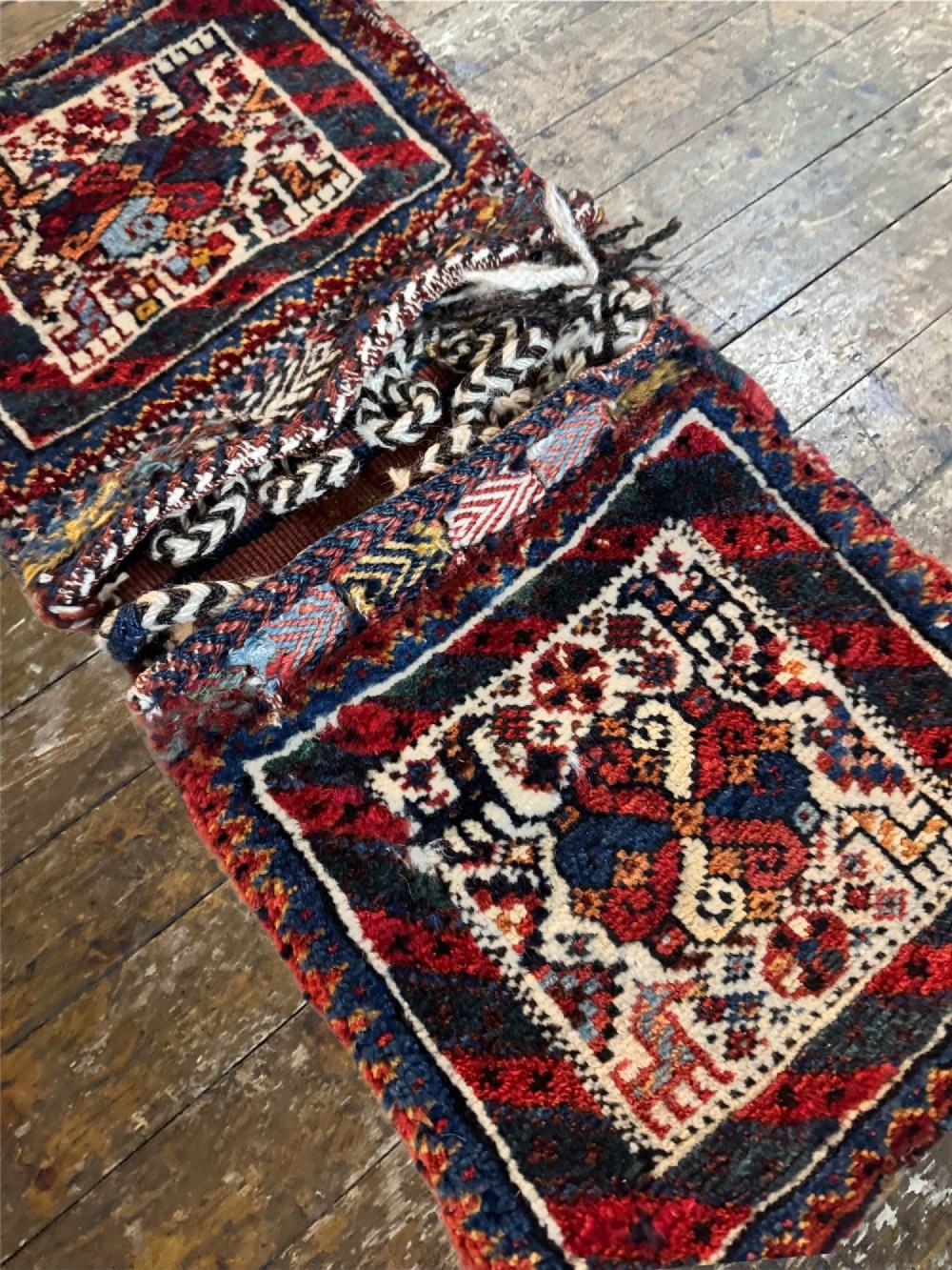 An antique handwoven Qashqai wool Khorjin double saddlebag featuring geometric medallions in red, navy, and cream with braided closure loops. View VI