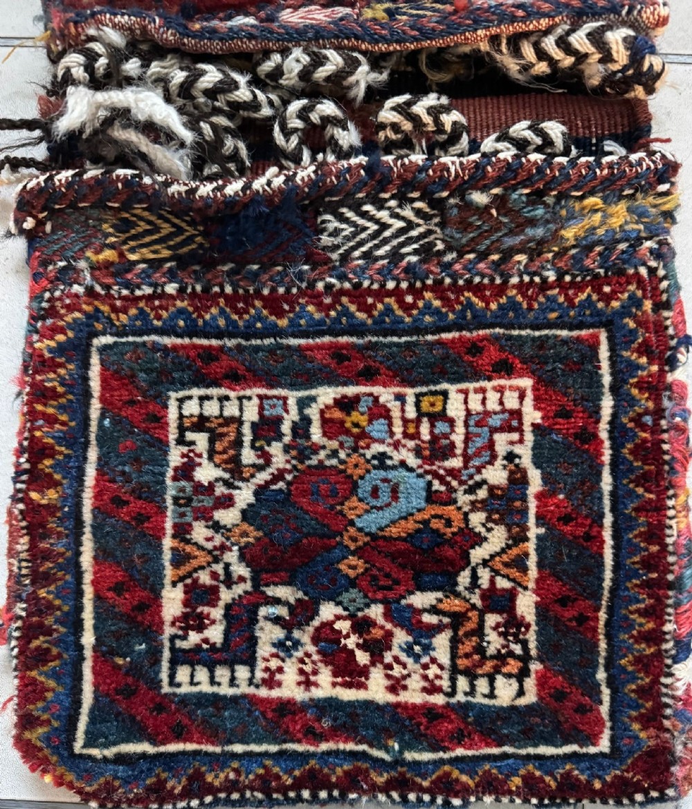 An antique handwoven Qashqai wool Khorjin double saddlebag featuring geometric medallions in red, navy, and cream with braided closure loops. View VII