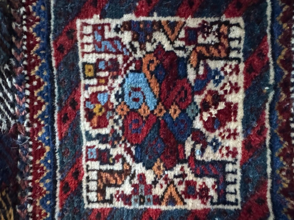 An antique handwoven Qashqai wool Khorjin double saddlebag featuring geometric medallions in red, navy, and cream with braided closure loops. View XII