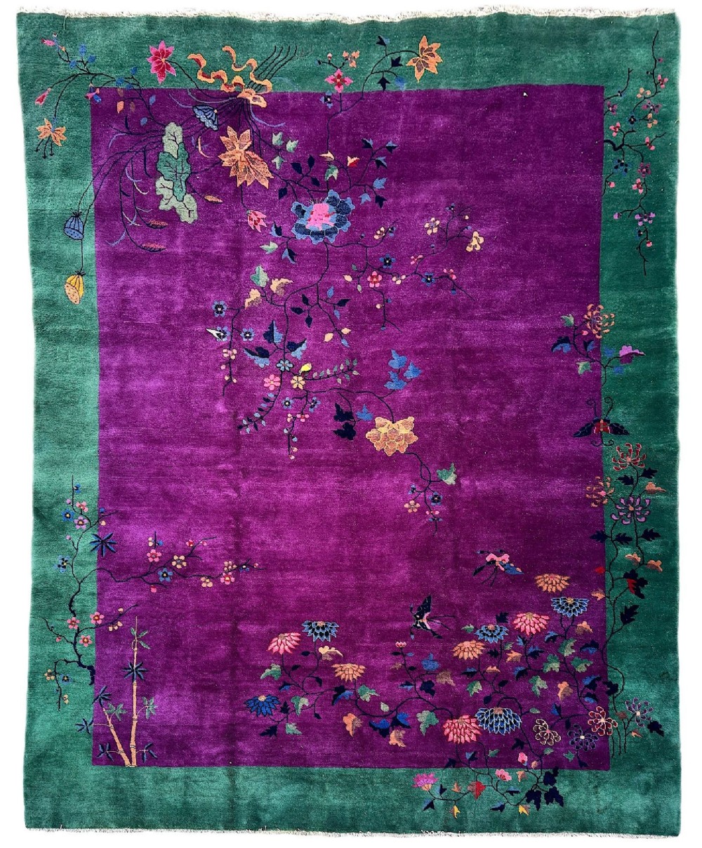 A large hand-knotted wool carpet featuring a vibrant magenta central field framed by a rich jade green border with asymmetrical floral and bamboo motifs.