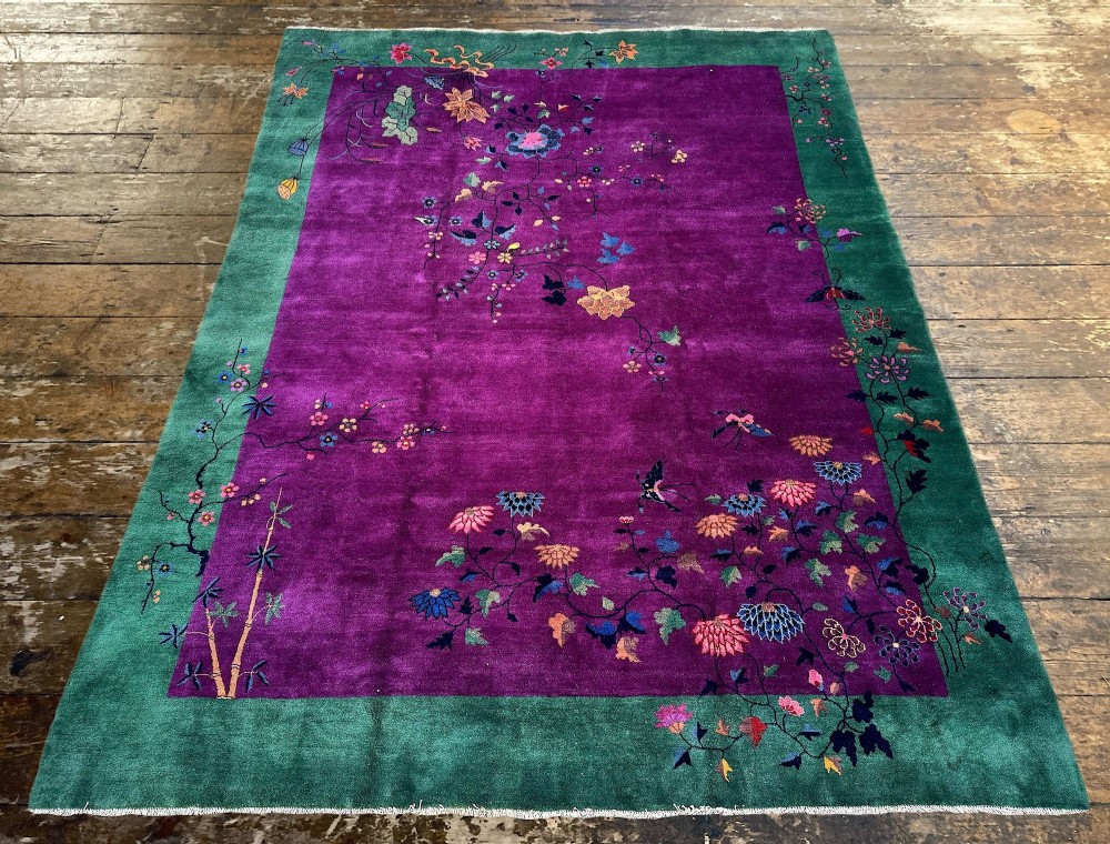 A large hand-knotted wool carpet featuring a vibrant magenta central field framed by a rich jade green border with asymmetrical floral and bamboo motifs. View IV