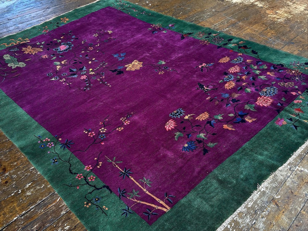 A large hand-knotted wool carpet featuring a vibrant magenta central field framed by a rich jade green border with asymmetrical floral and bamboo motifs. View V