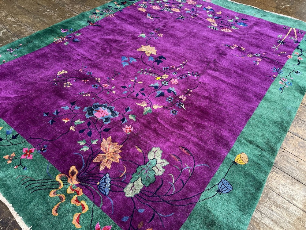 A large hand-knotted wool carpet featuring a vibrant magenta central field framed by a rich jade green border with asymmetrical floral and bamboo motifs. View VI