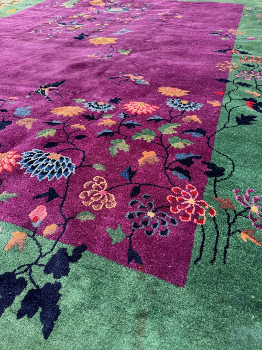 A large hand-knotted wool carpet featuring a vibrant magenta central field framed by a rich jade green border with asymmetrical floral and bamboo motifs. View X