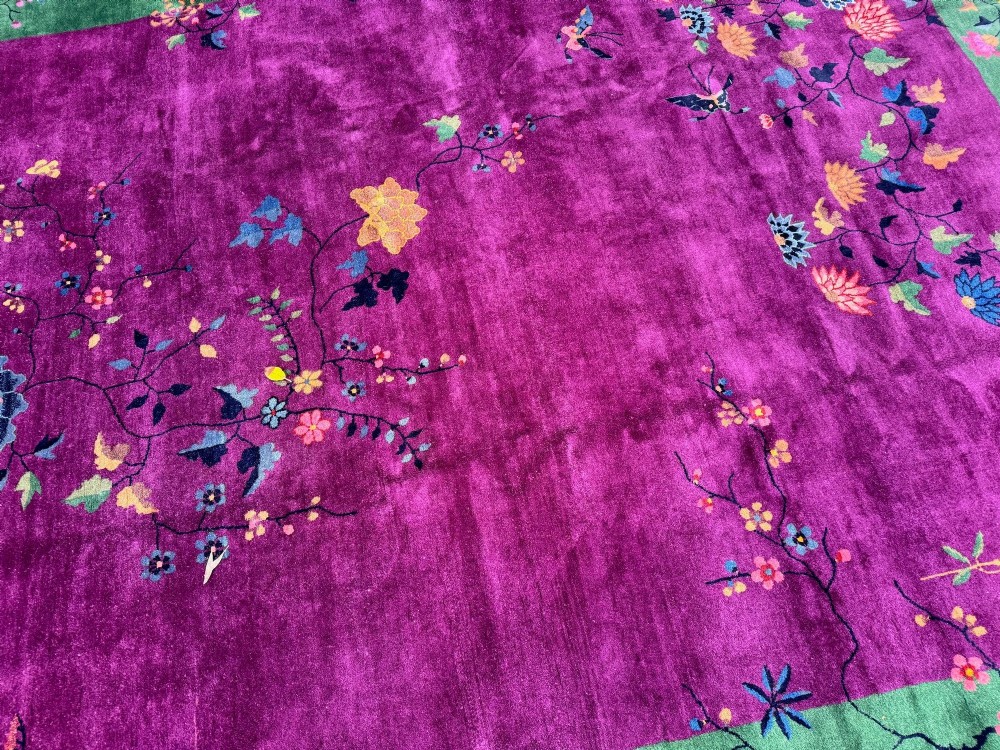 A large hand-knotted wool carpet featuring a vibrant magenta central field framed by a rich jade green border with asymmetrical floral and bamboo motifs. View XII